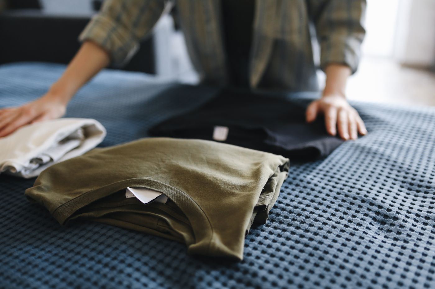 Hands neatly folding freshly laundered t-shirts on a bed