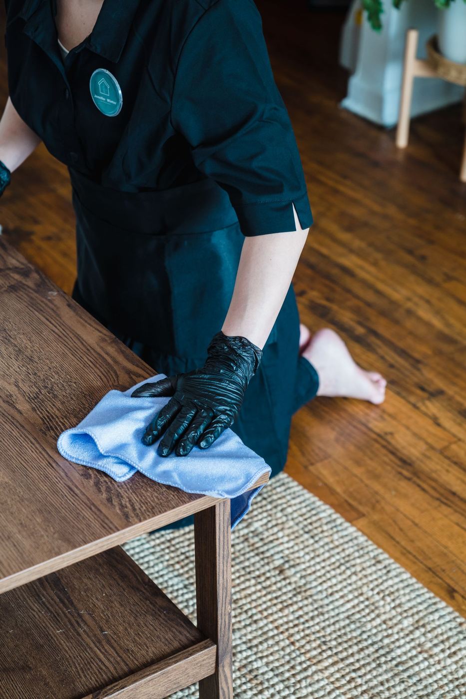 Housekeeper in black gloves wiping down a wooden coffee table during a standard house cleaning