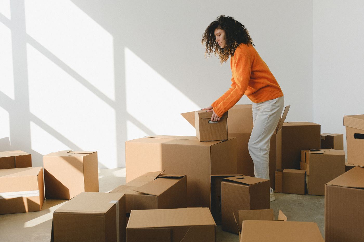 Woman unpacking cardboard moving boxes in a bright, empty apartment