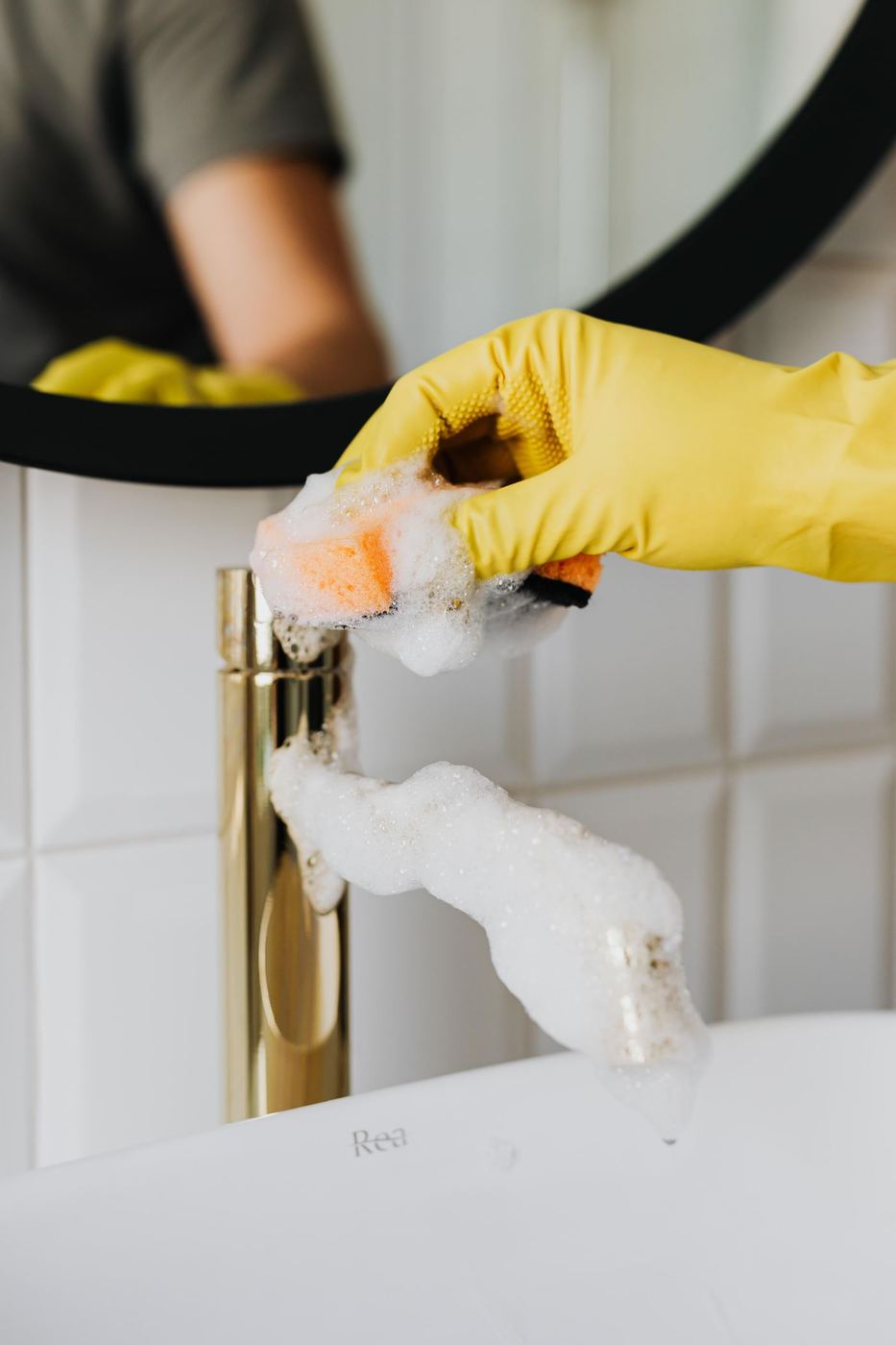 Gloved hand polishing a gold bathroom faucet with a sponge
